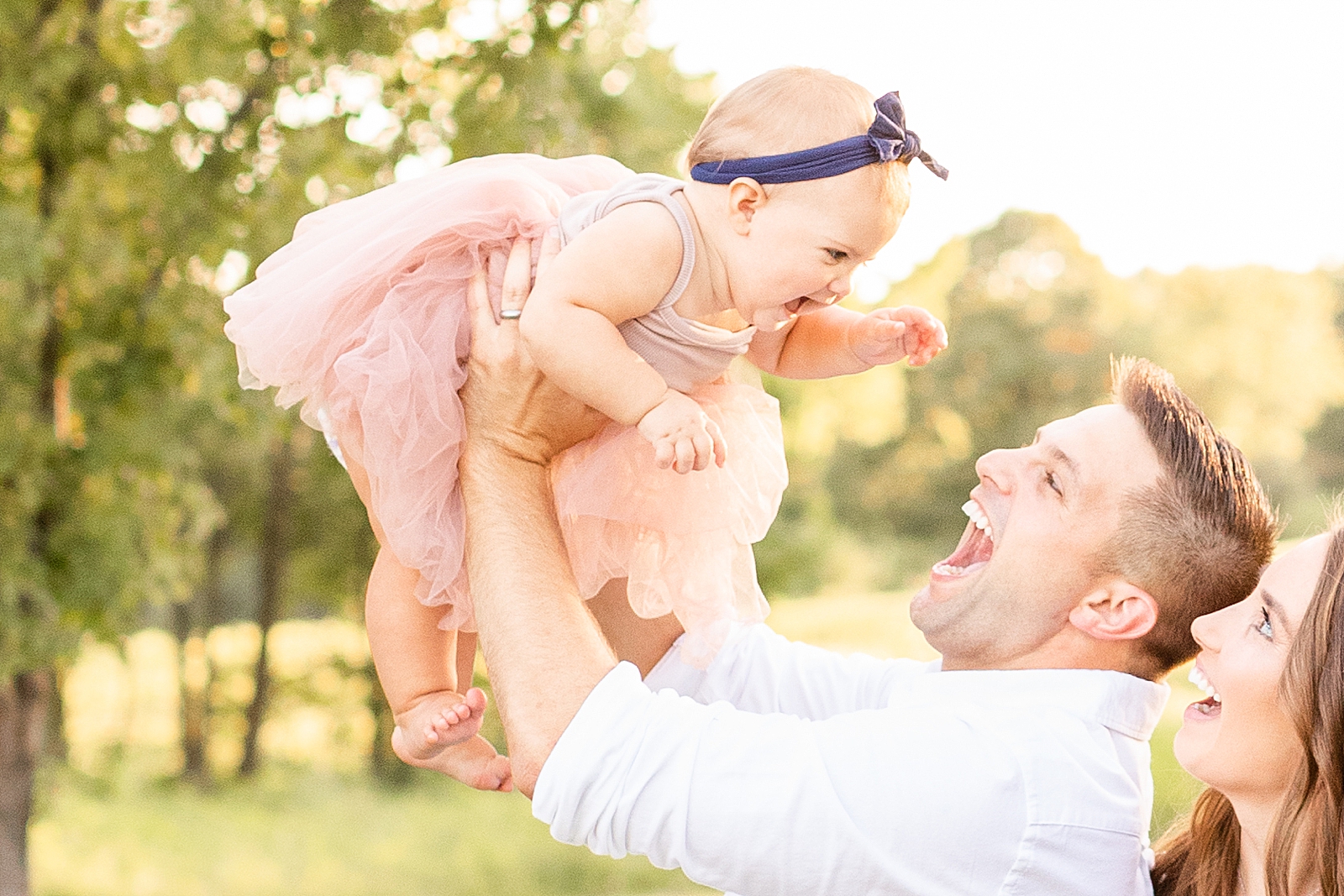 dad holding up baby girl in pink tutu while baby gives big smiles