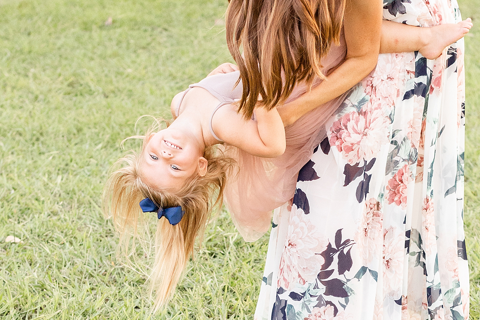 little girl in pink tutu smiles big as she is flipped upside down by her mom during family session