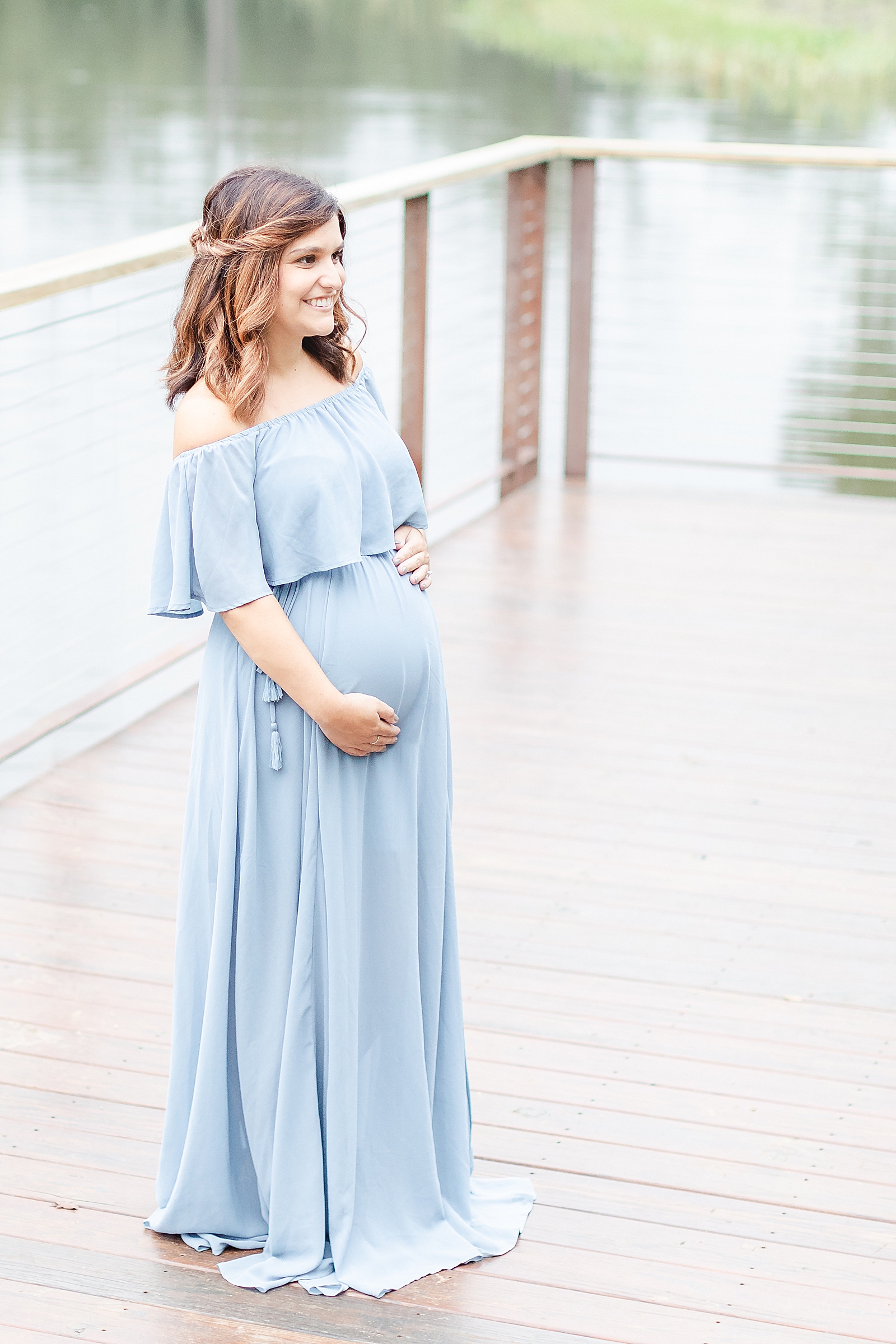 mom wearing off the shoulder blue gown holding baby bump smiling off camera during maternity photos