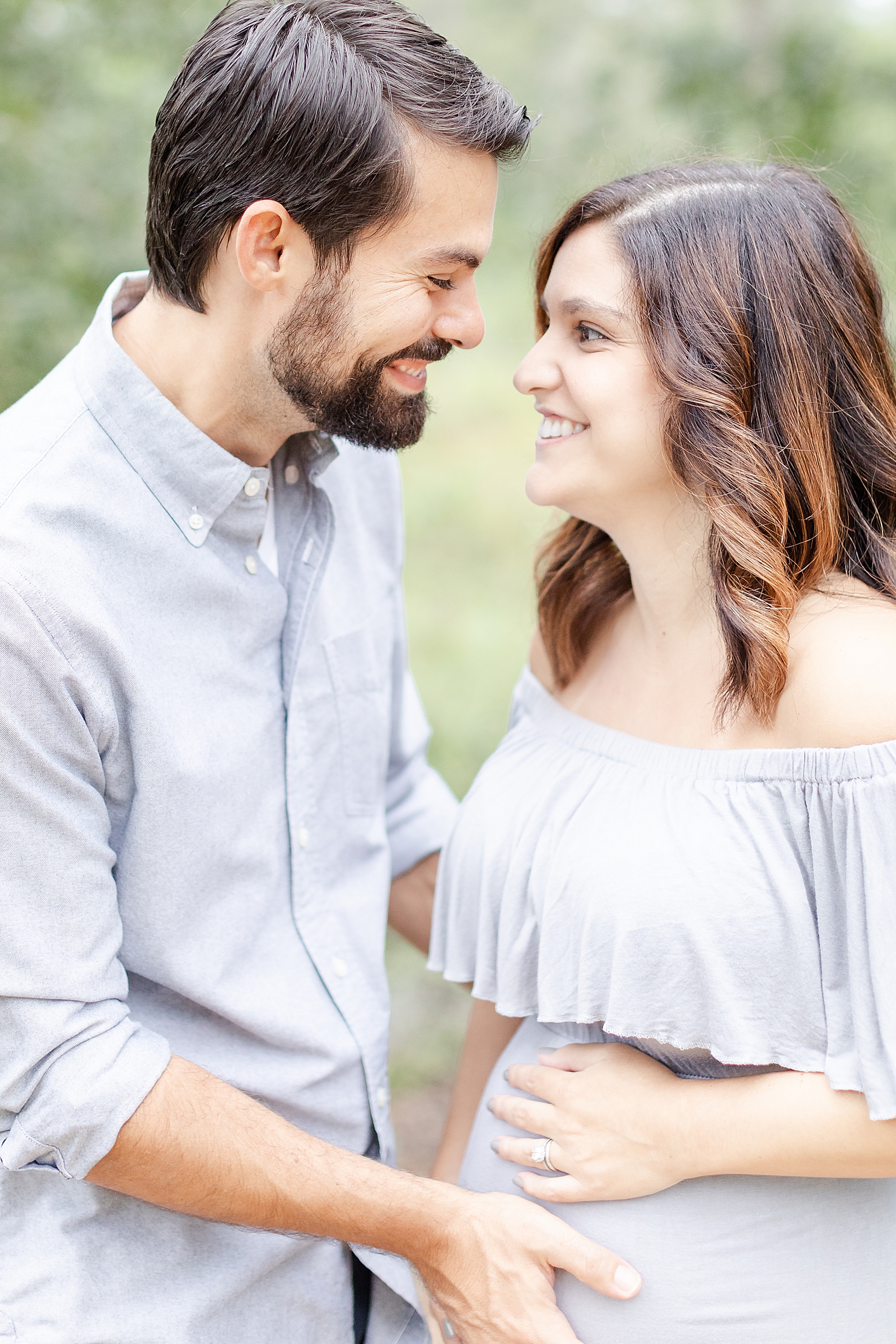 huabdna and wife smiling at each other while both holding on to baby bump during their rainbow baby maternity session