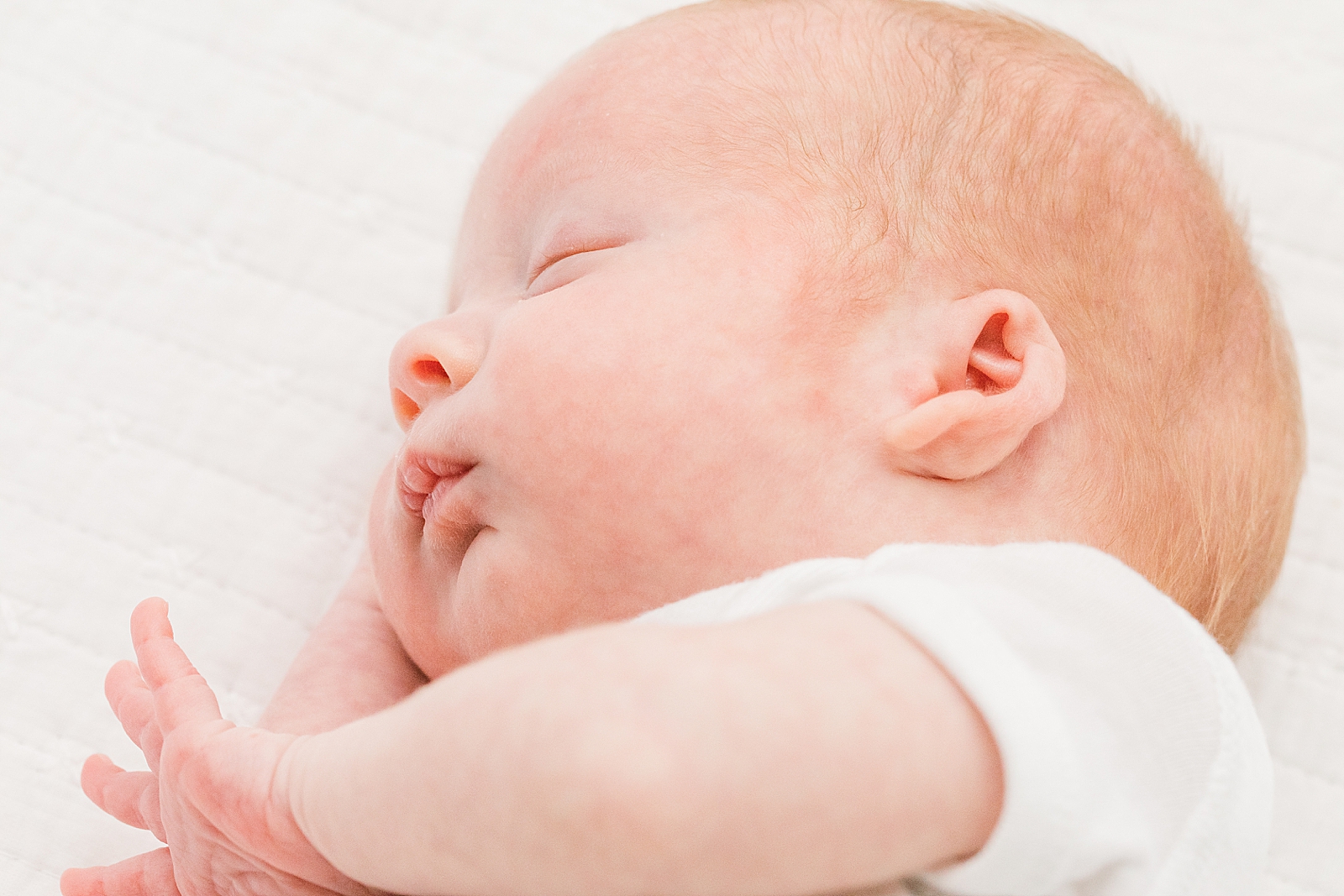 twin boy asleep wearing white onesie on a white bed during newborn photos