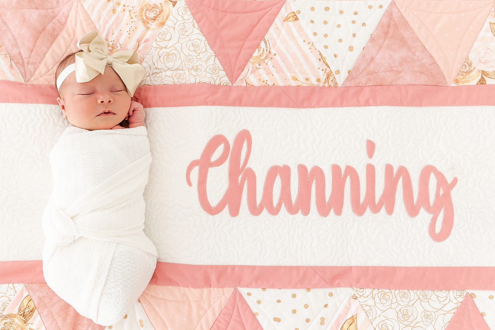 Baby Channing custom pink white and gold newborn quilt with baby in white swaddle and gold bow asleep