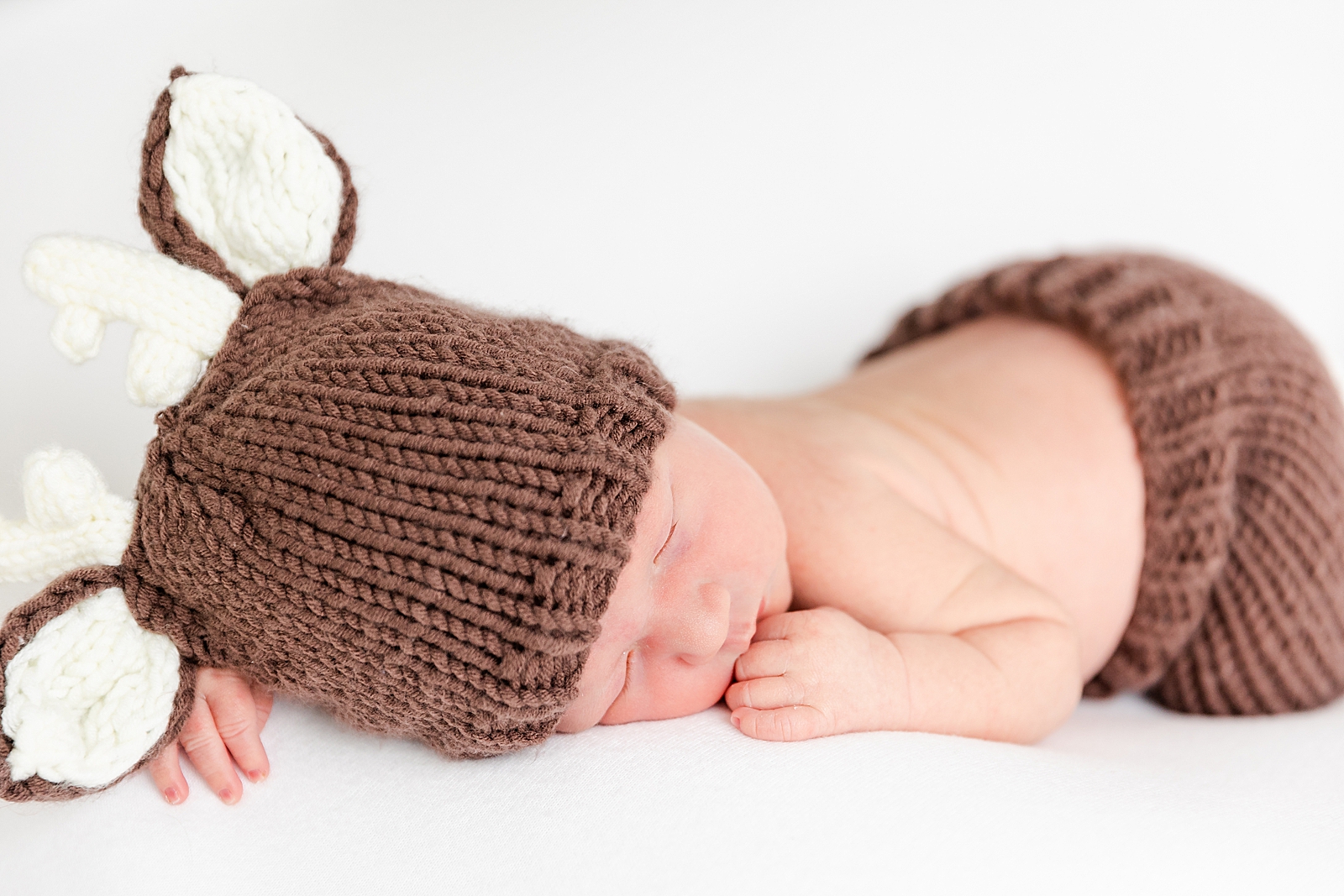 Newborn baby dressed in deer outfit sleeping on tummy on a white backdrop