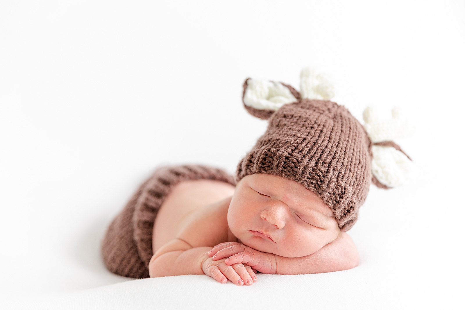 Newborn dressed in deer outfit asleep on his tummy in a posed photo on a white background