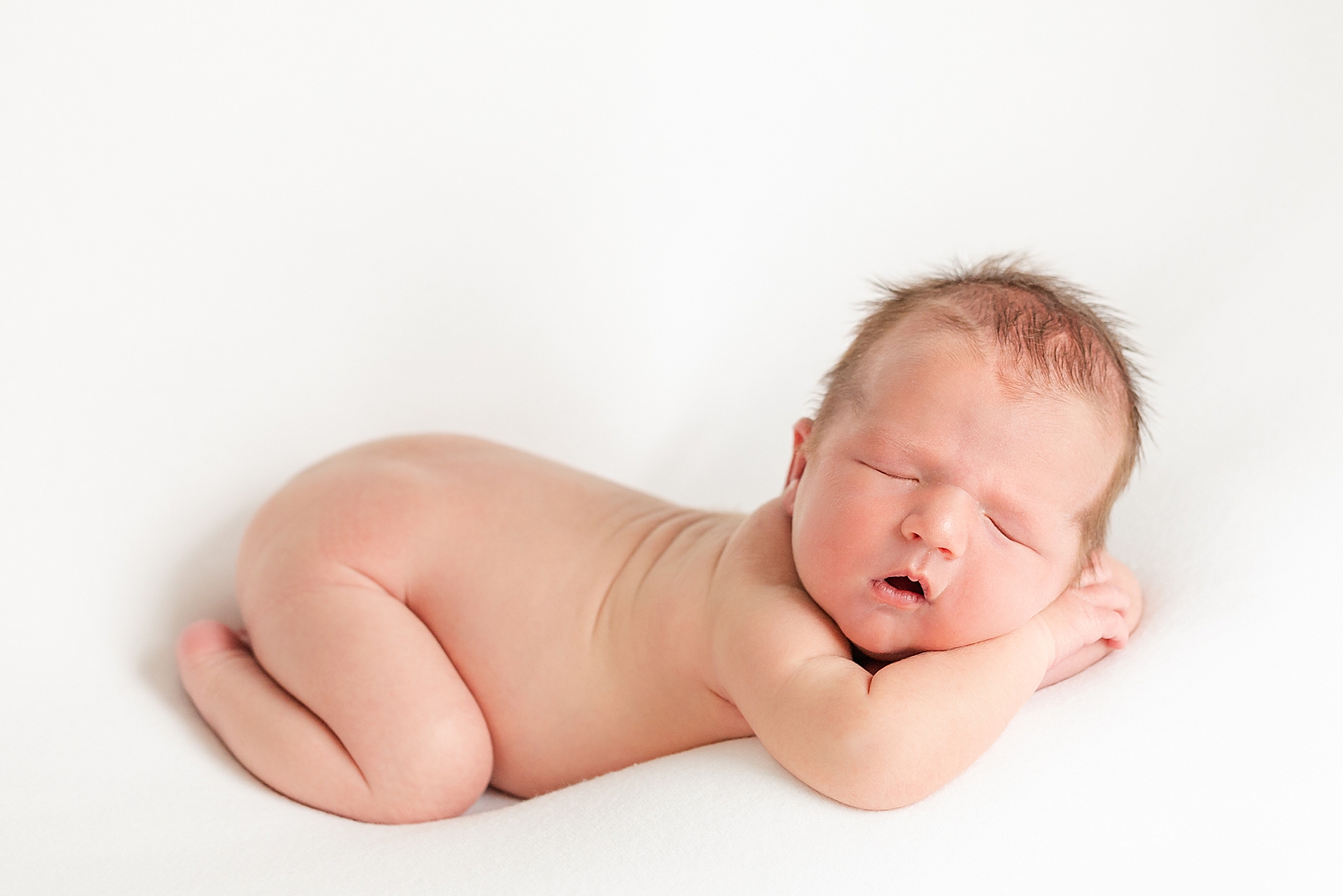 Posed newborn photo of sleeping baby on tummy with face resting on arms naked
