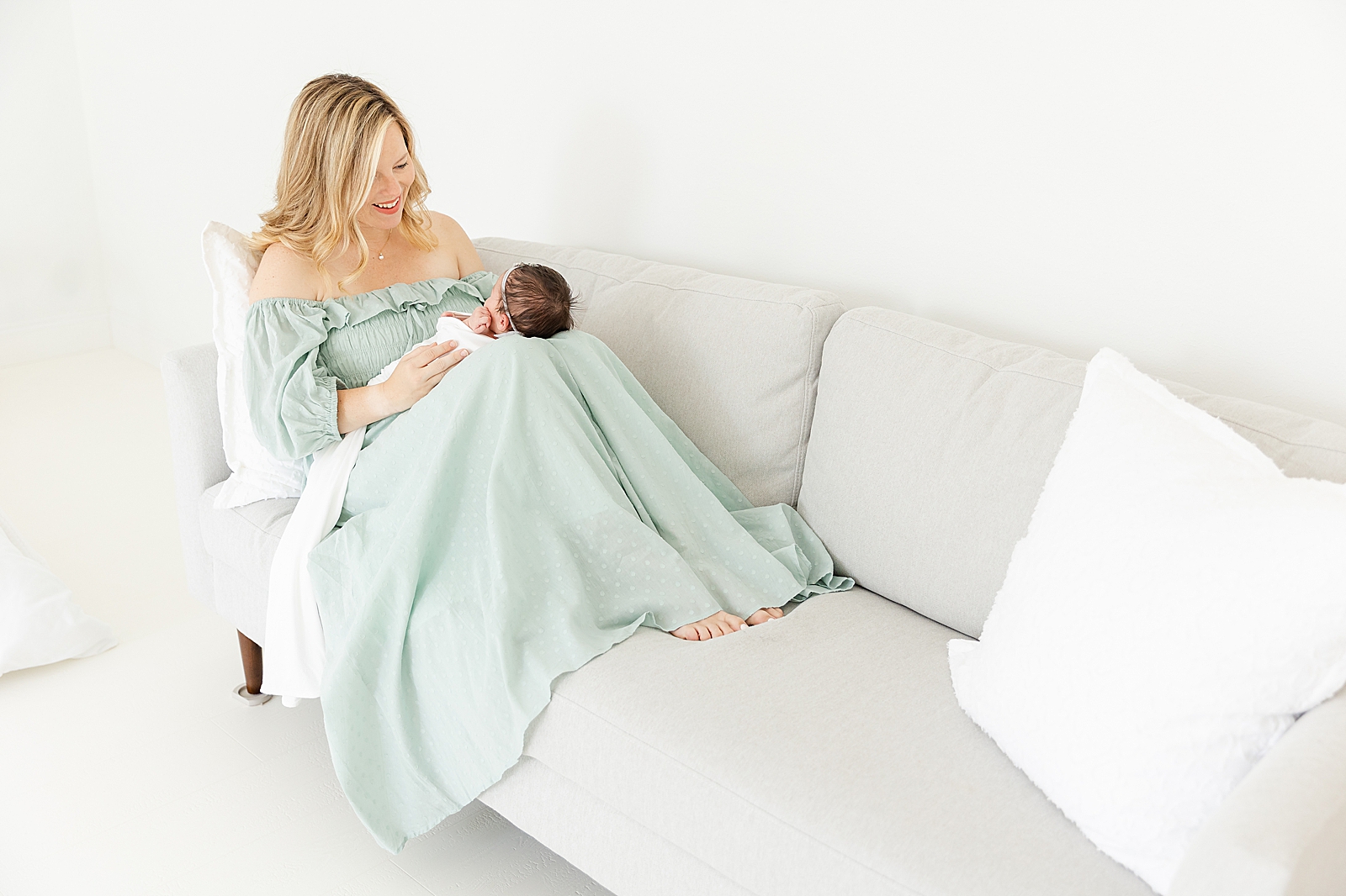 Mom on couch holding baby in white swaddle at lifestyle newborn session