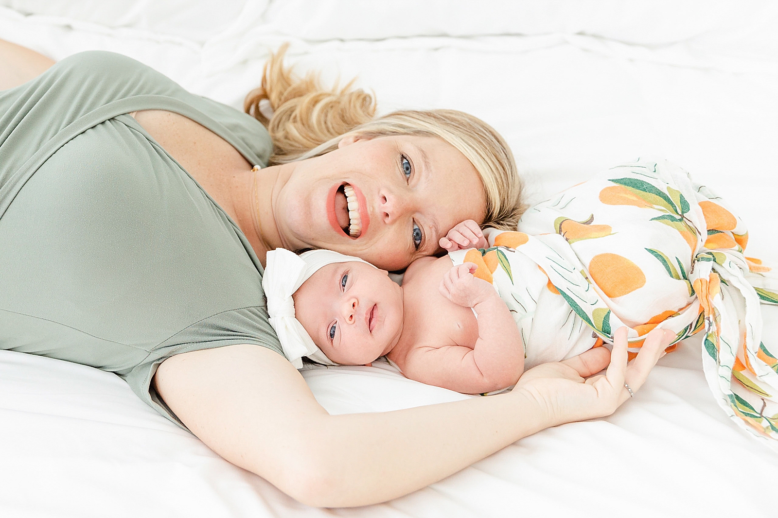 Swaddled baby and mom cheek to cheek smiling at camera at newborn session