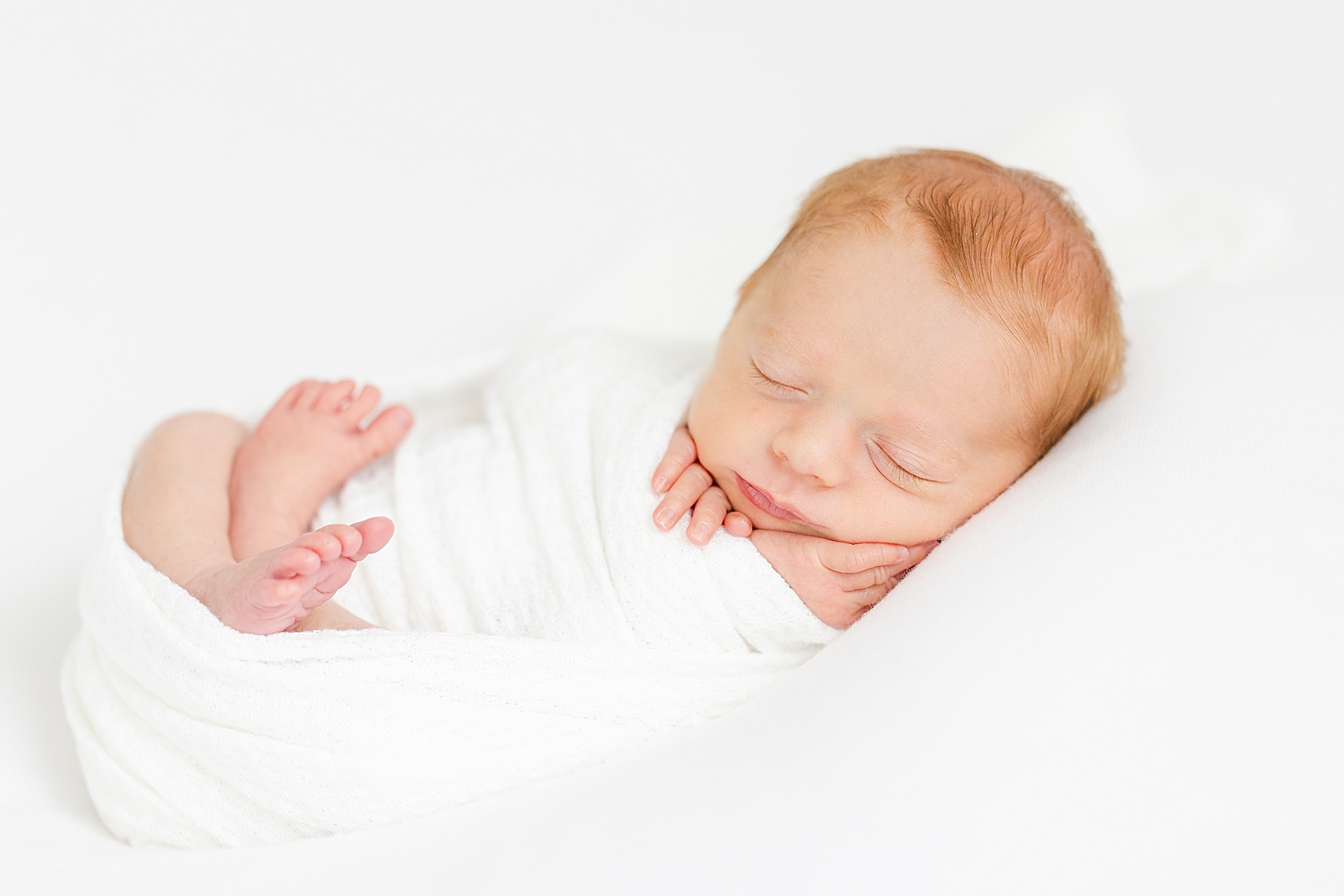 Studio Newborn Session of posed baby in white swaddle asleep with feet out
