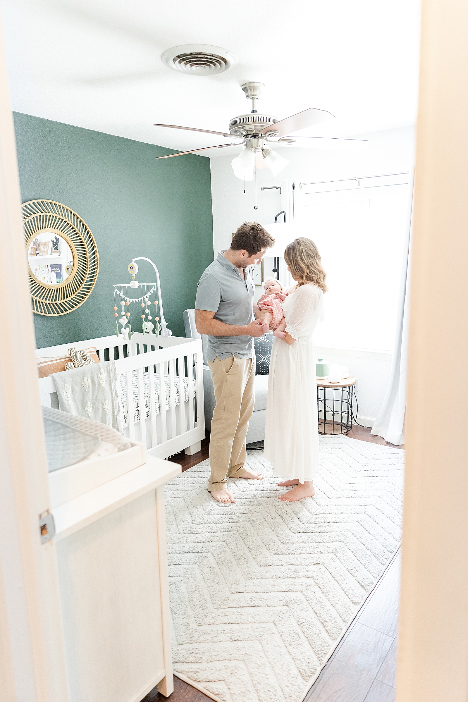 mom and dad holding baby in the center of the nursery looking through the door