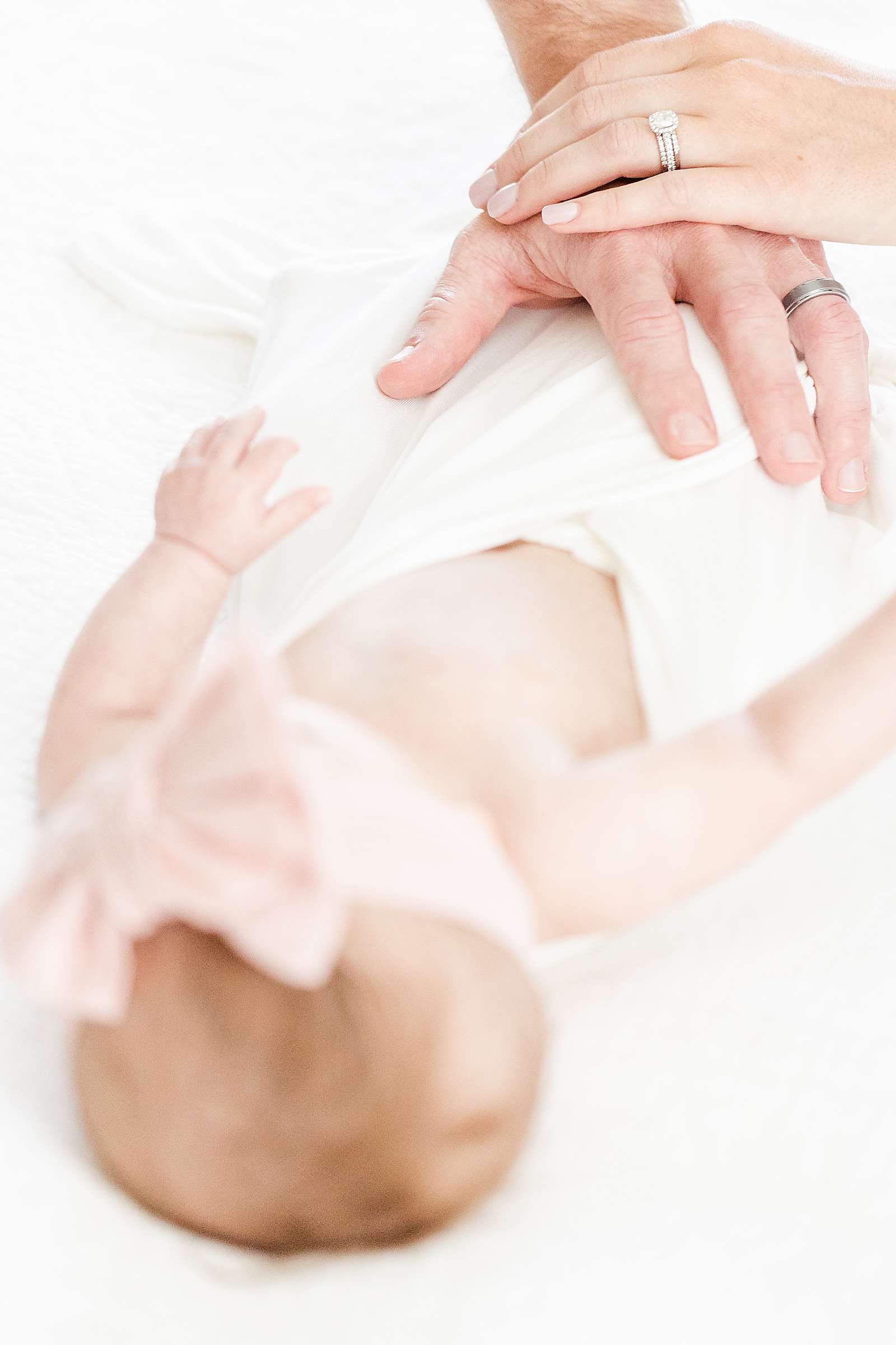 mom and dads hands together on top of baby with hands and wedding rings in focus and baby out of focus
