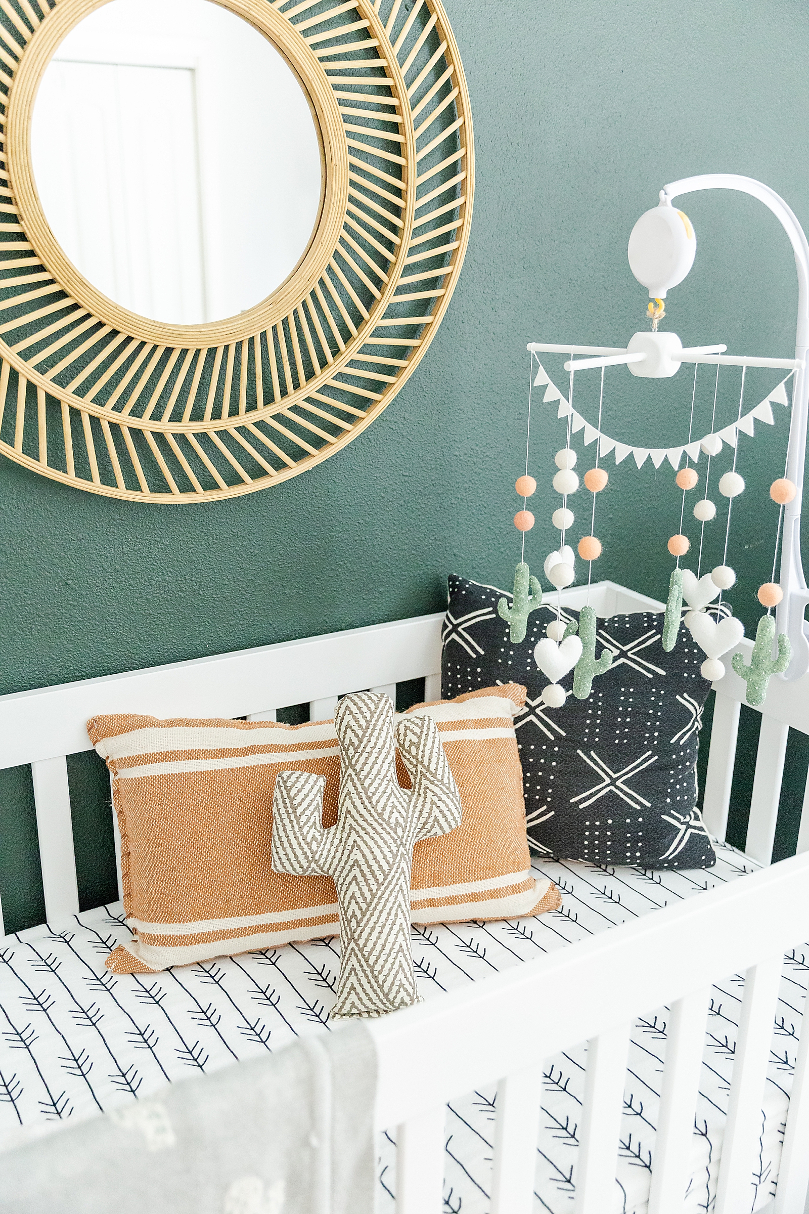 cactus theme nursery crib with dark green wall and gold round mirror with cactus mobile and cactus blanket and cactus pillow