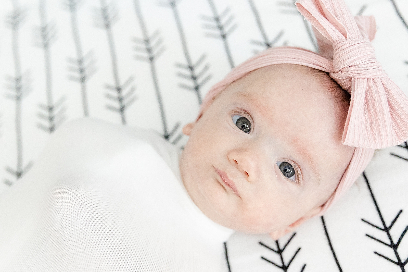 Lifestyle Newborn Photos baby in crib swaddles with big pink bow eyes open looking directly at camera