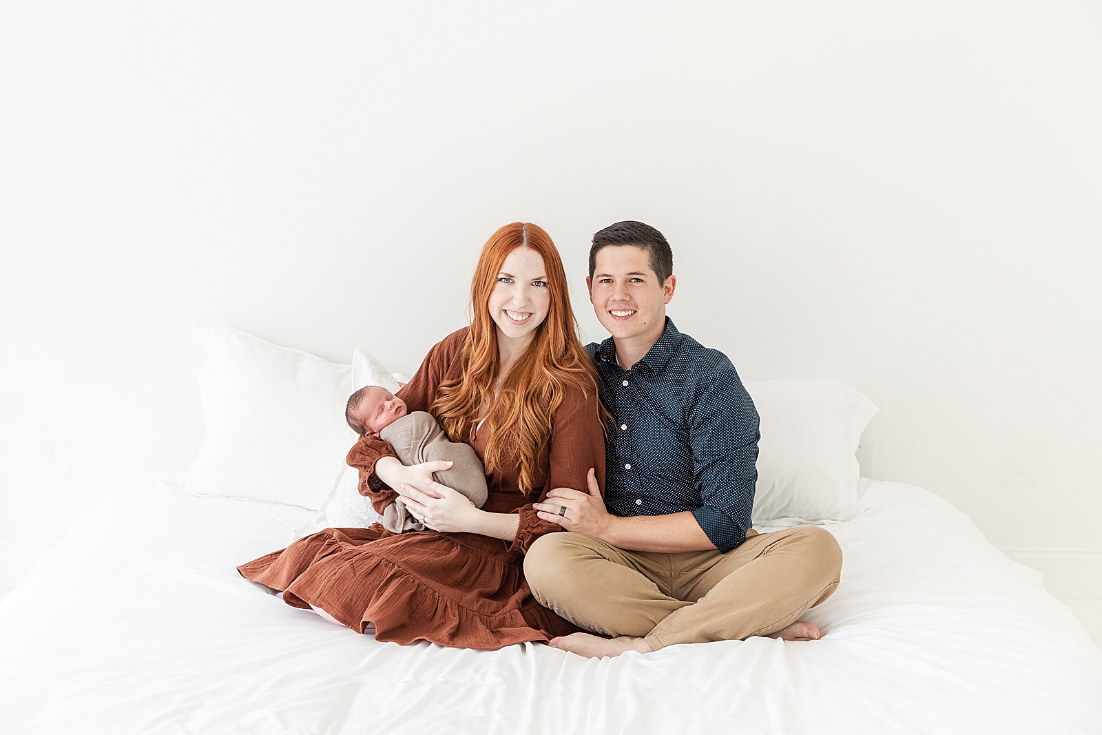 Newborn Photos Mom and dad sitting on bed holding baby at newborn session