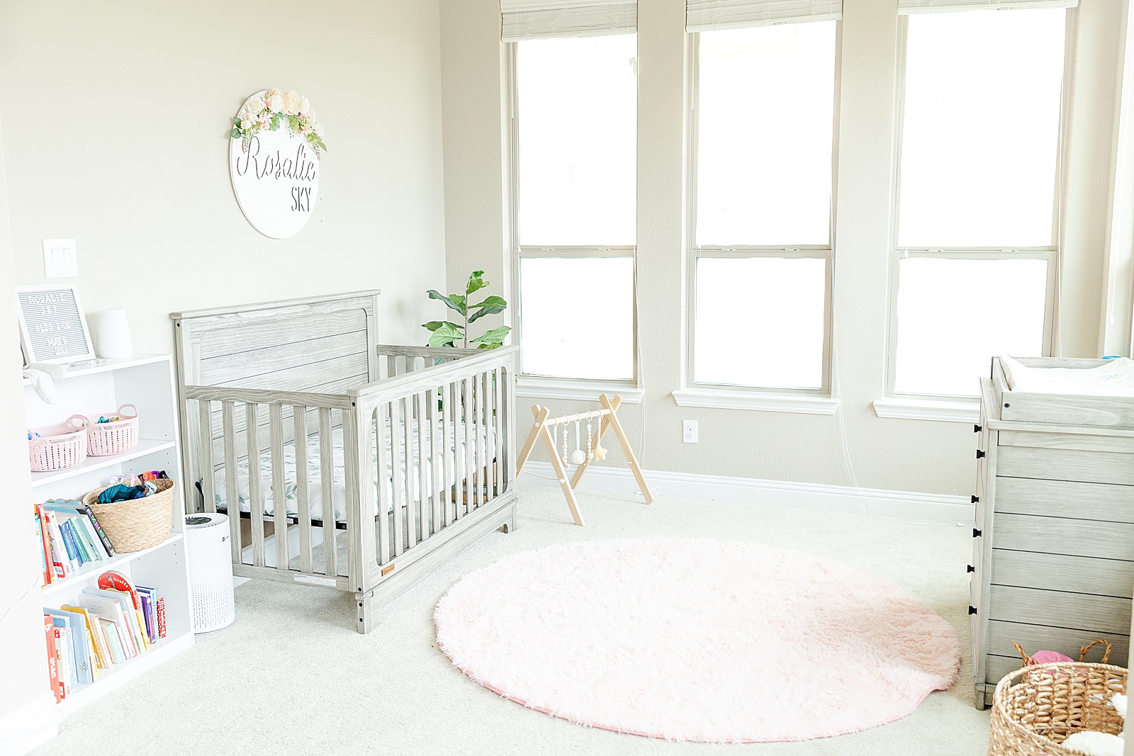 pulled back shot of a neutral baby girl nursery with pink accents