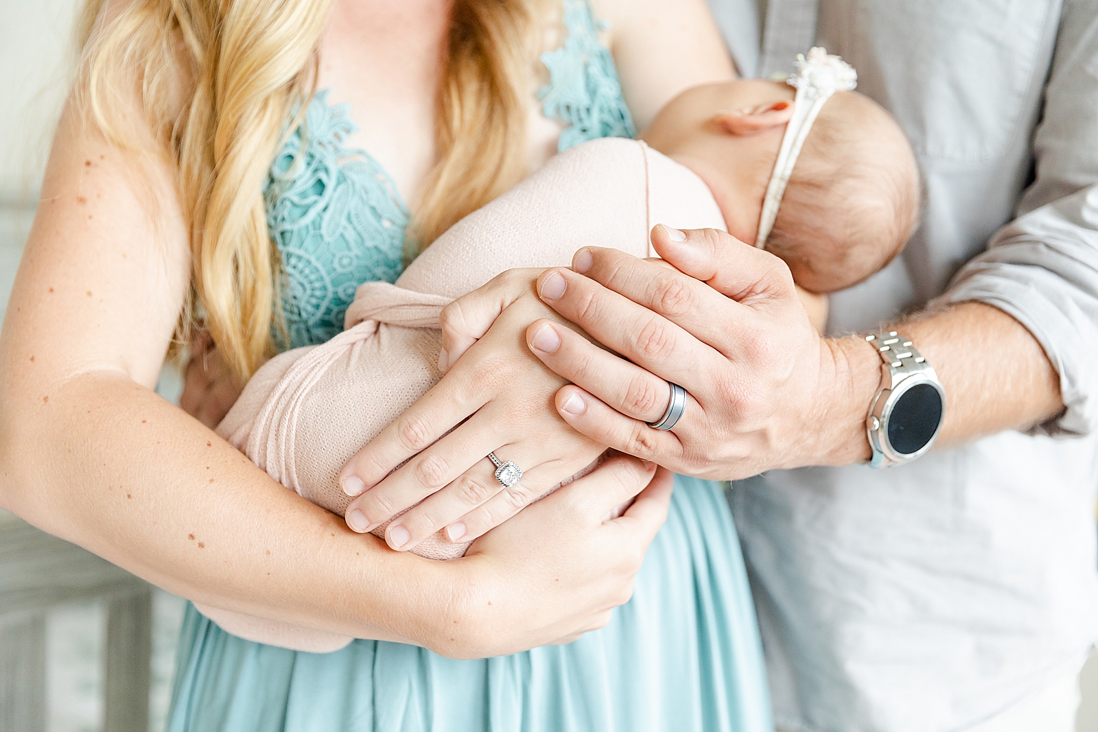Mom and dad holding on to newborn baby girl with wedding rings
