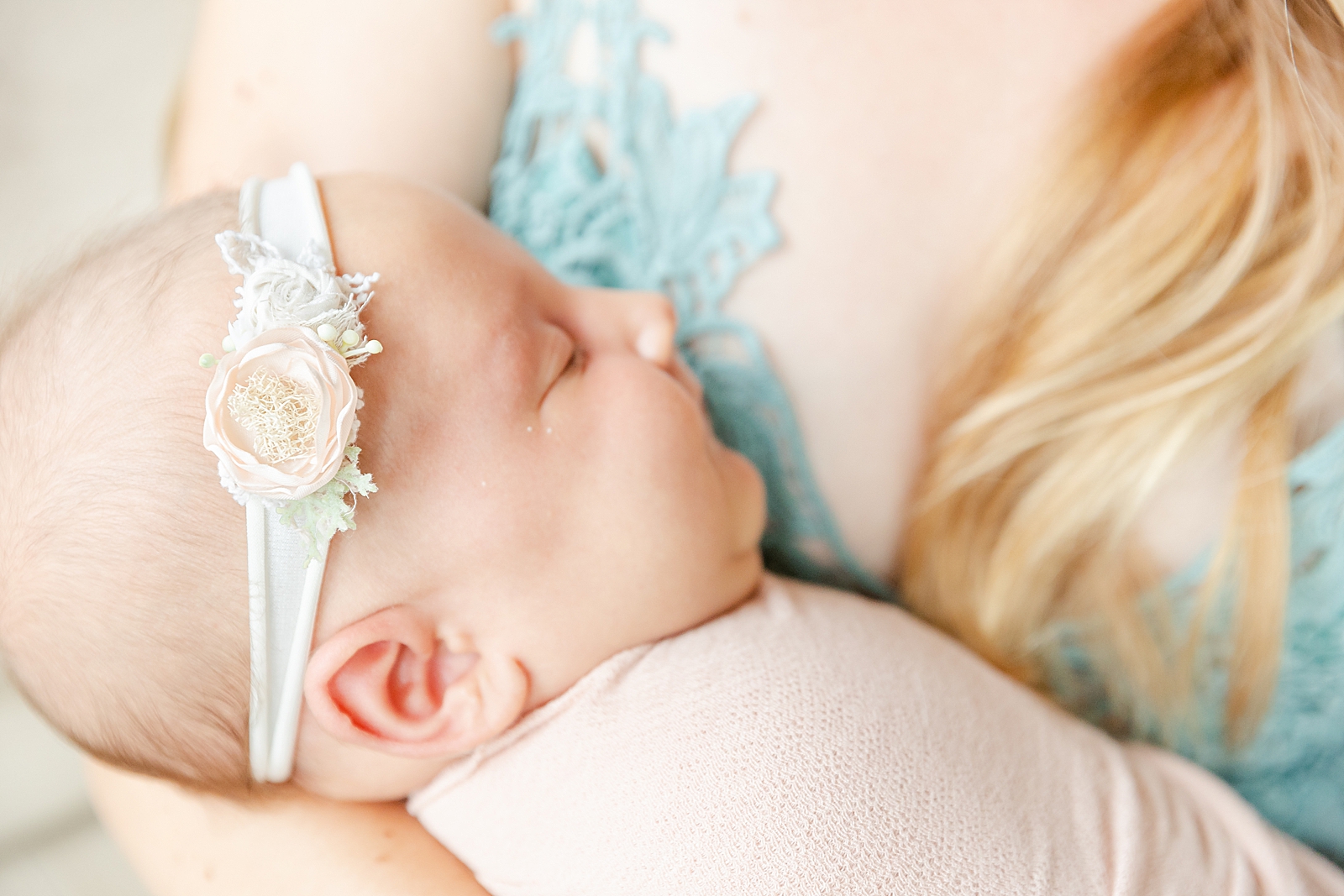 In-home newborn session baby girl wearing headband with flowers in her moms arms