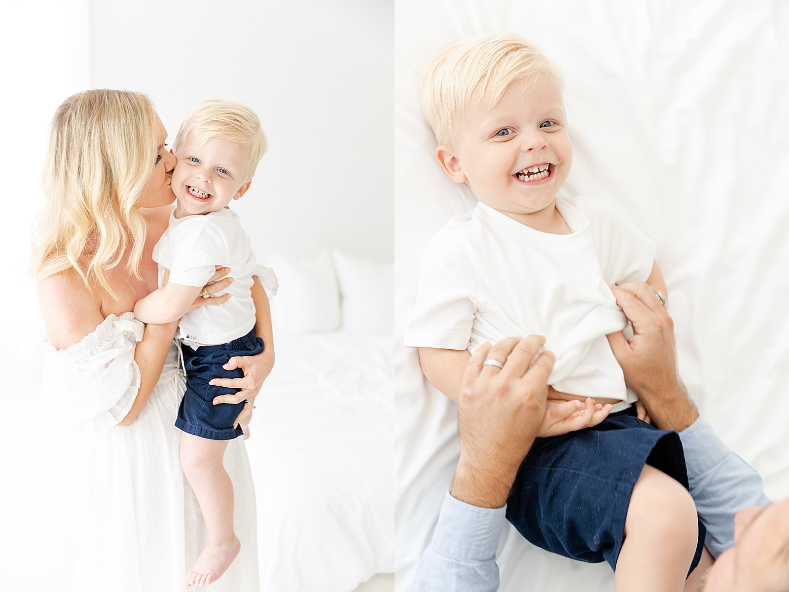 studio family session mom with blonde hair in white dress kissing toddler on the cheek with toddler smiling and picture of dad ticking toddler on the bed with a big smile