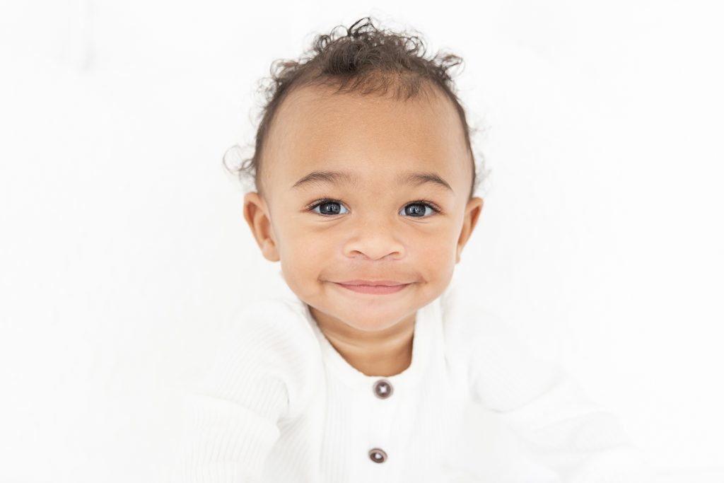 one year old boy smiling at the camera with white backdrop 
