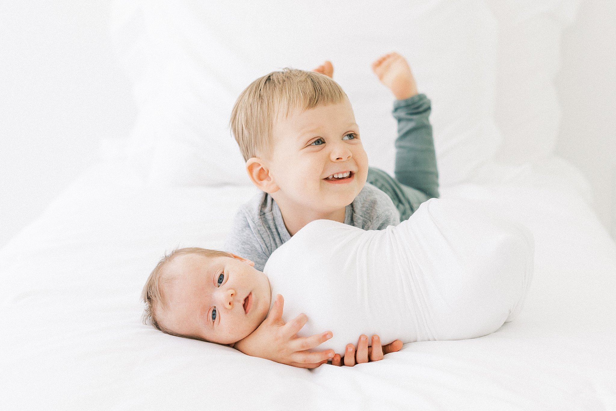 A young boy lays on a bed playing with his newborn baby sibling