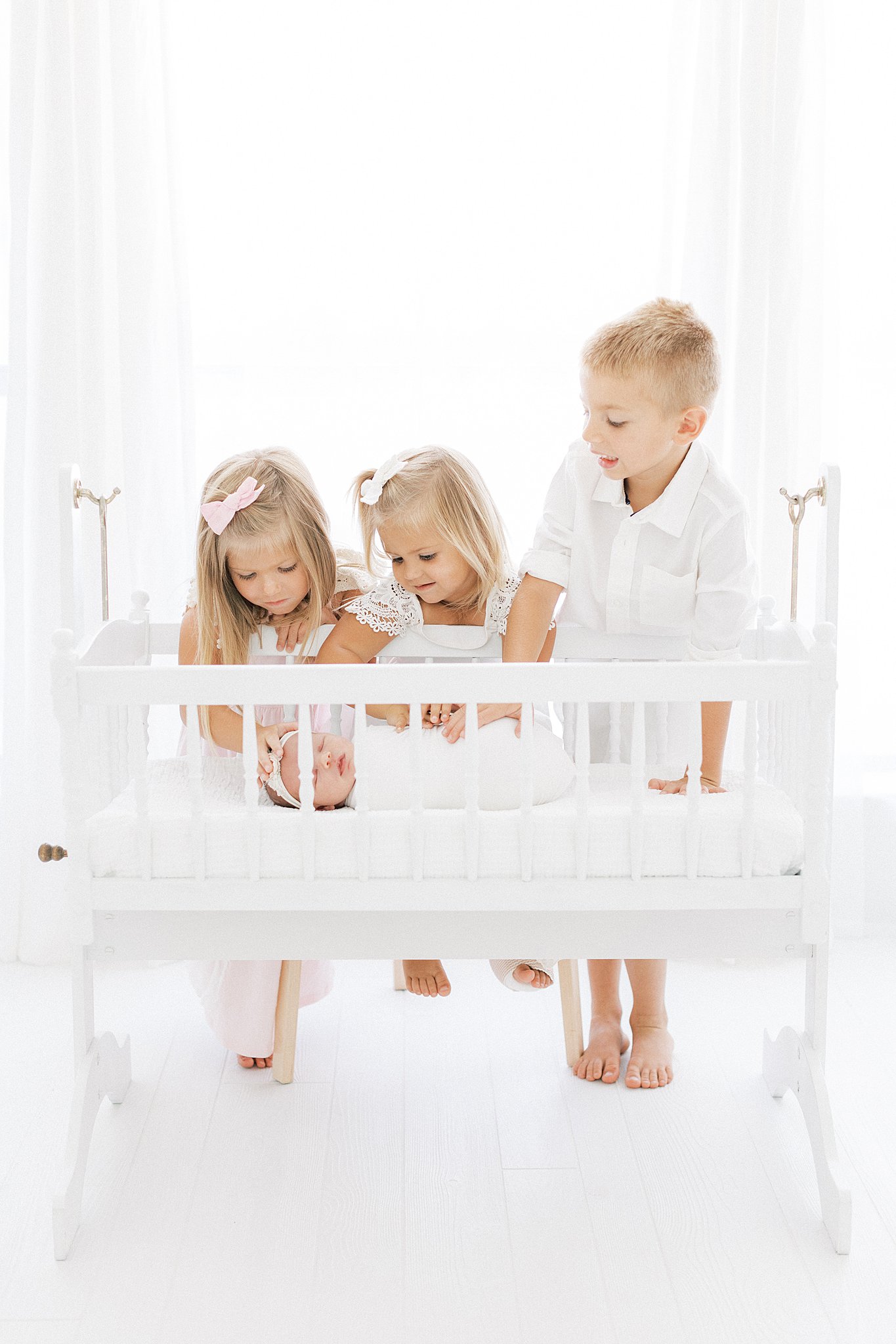 Three siblings stand over and reach into the crib of their newborn baby sister Dallas baby furniture stores