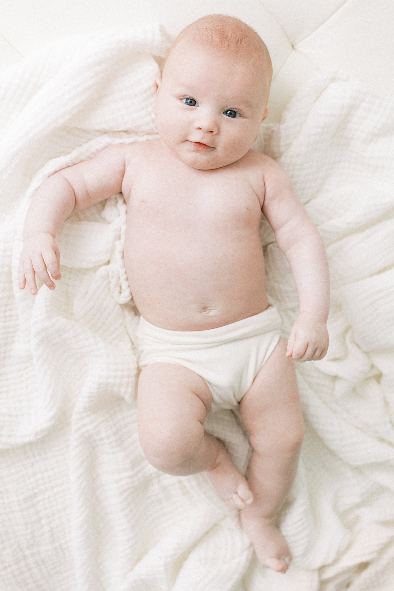 A newborn baby lays in cloth underwear on a white blanket with eyes open