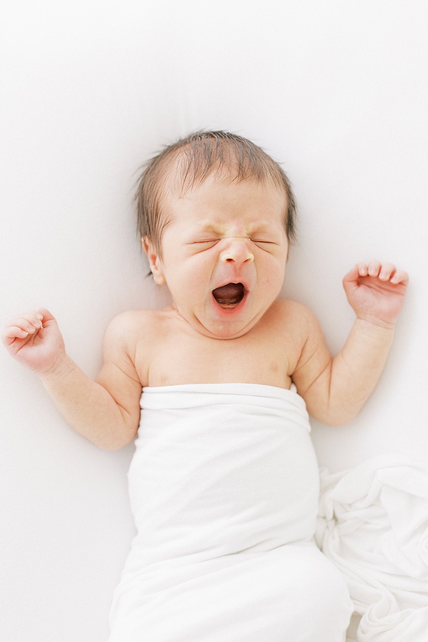 A newborn baby lets out a large yawn on a white bed