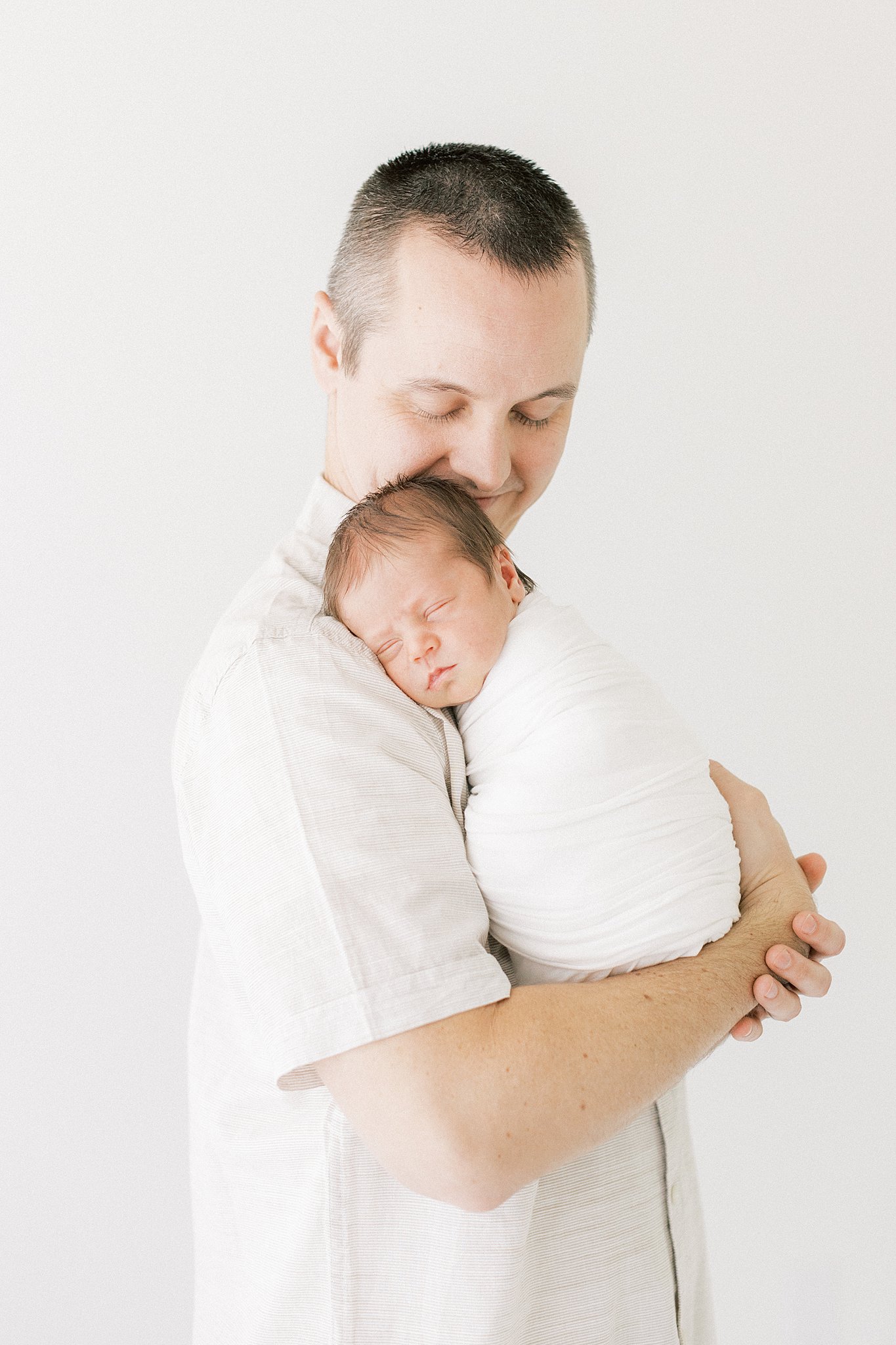 A new father in a white shirt holds his sleeping newborn on his shoulder layette dallas
