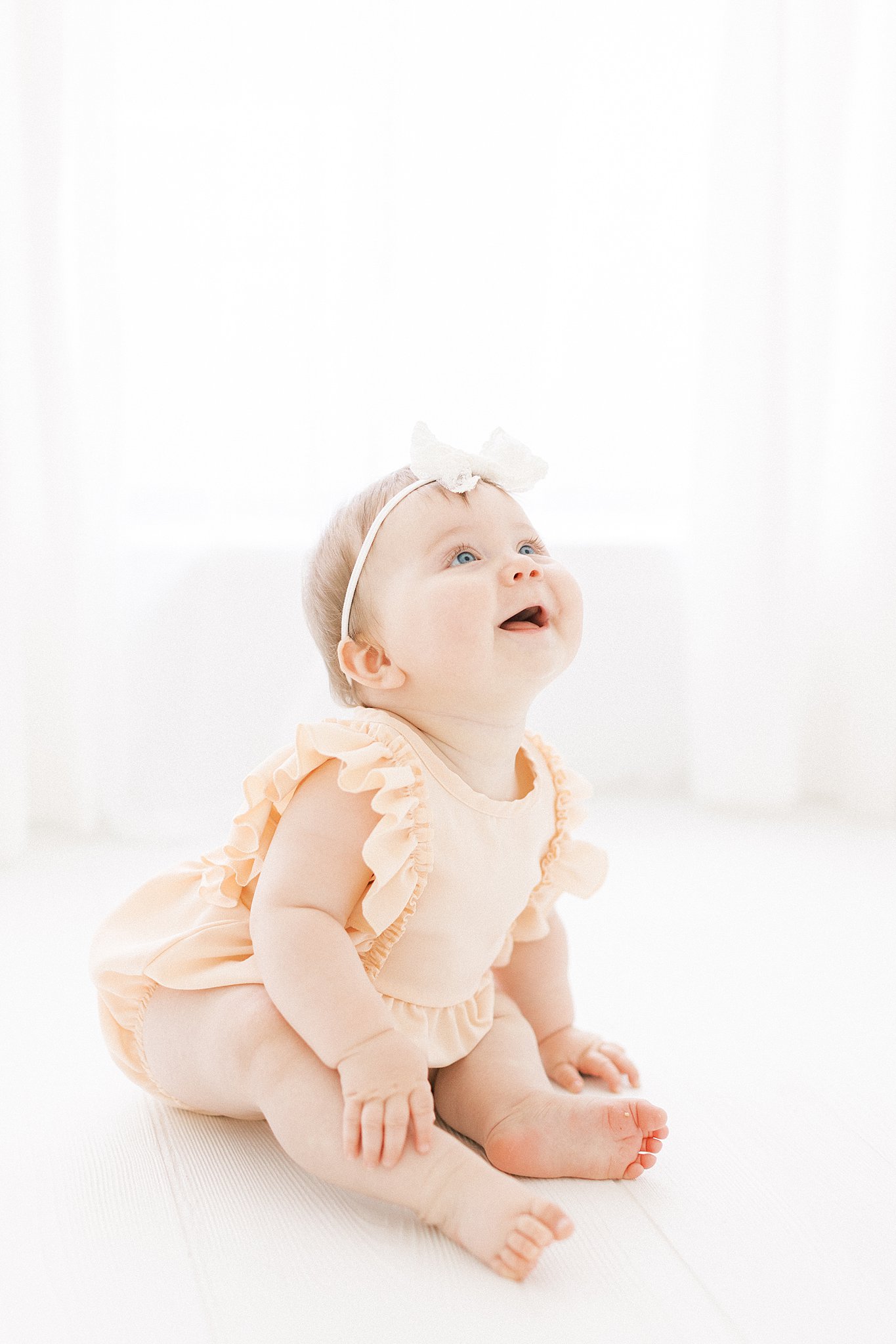 An infant baby girl sits in a studio in a peach onesie smiles up to the sky Dondolo Dallas