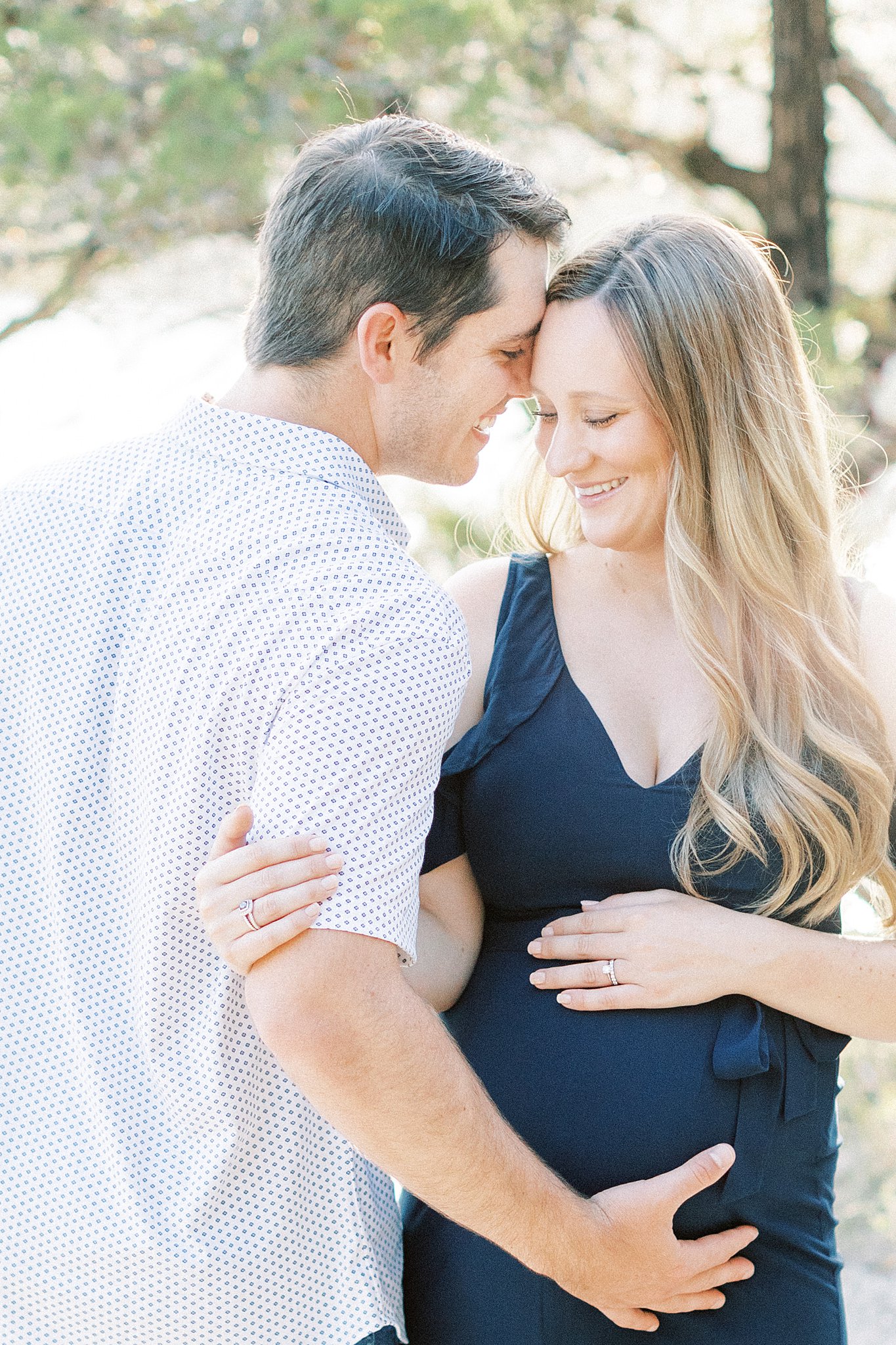 A mother to be laughs with her husband on a mountain path while they both hold the bump