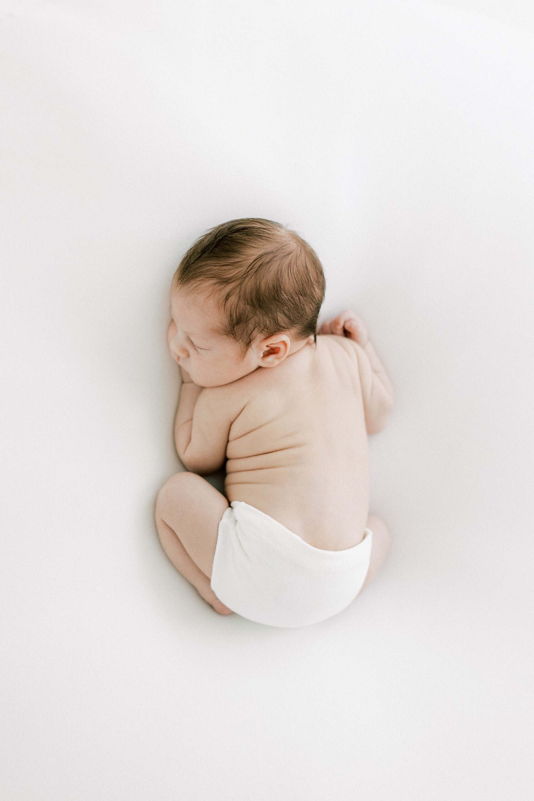 A newborn baby sleeps on its stomach on a white pad in a studio after meeting a Dallas Au Pair