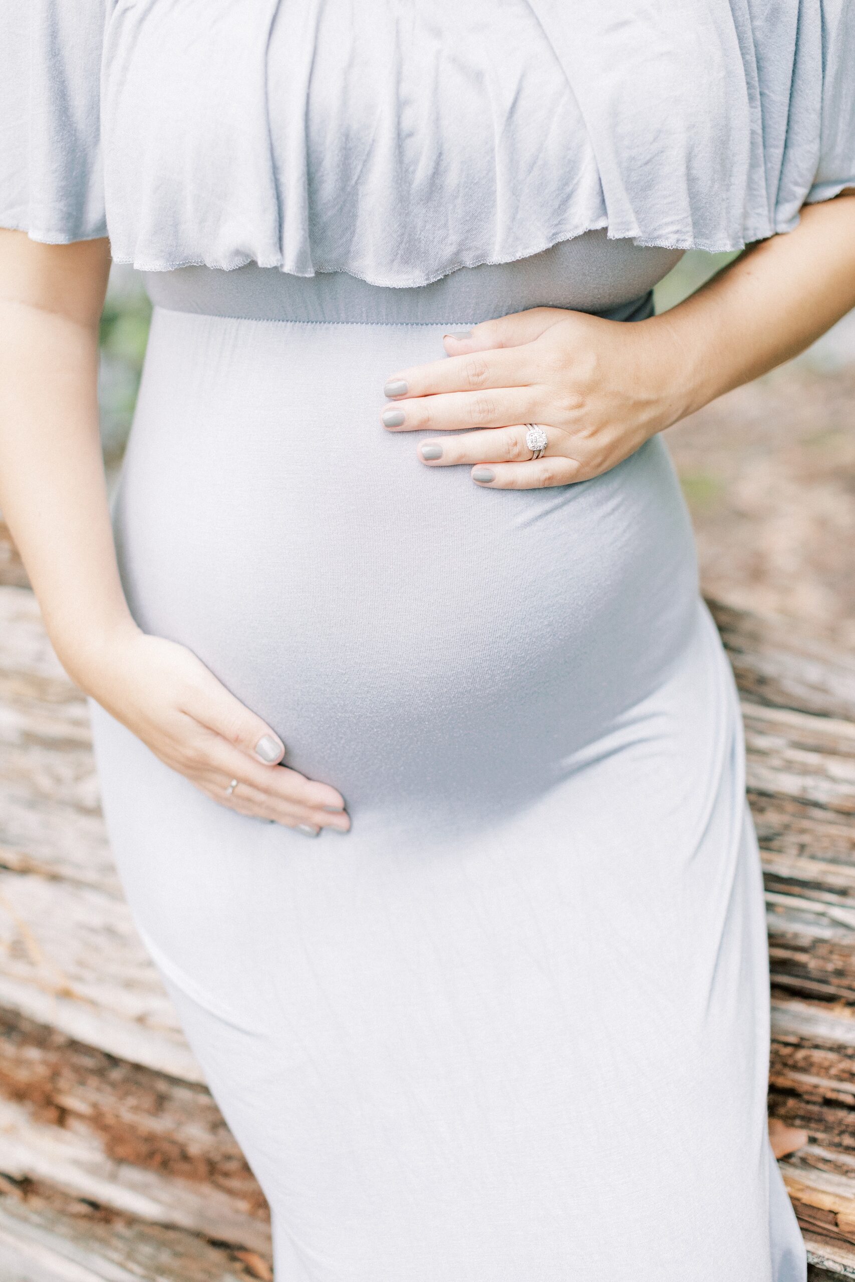 Details of a mother to be holding her bump while standing against a wooden fence in a blue maternity gown