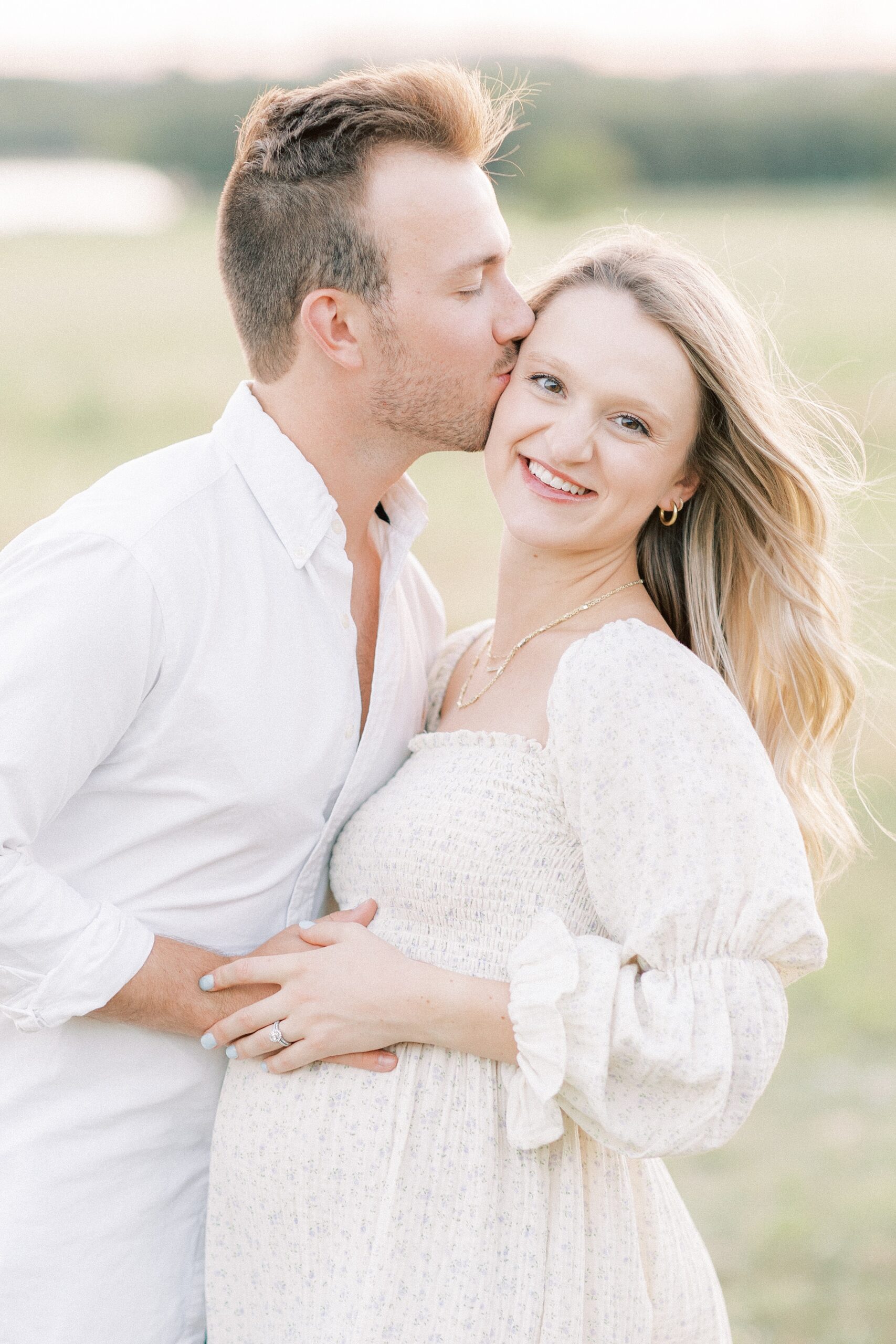 A husband kisses his pregnant wife while standing in a windy field after visiting Plano Birthplace